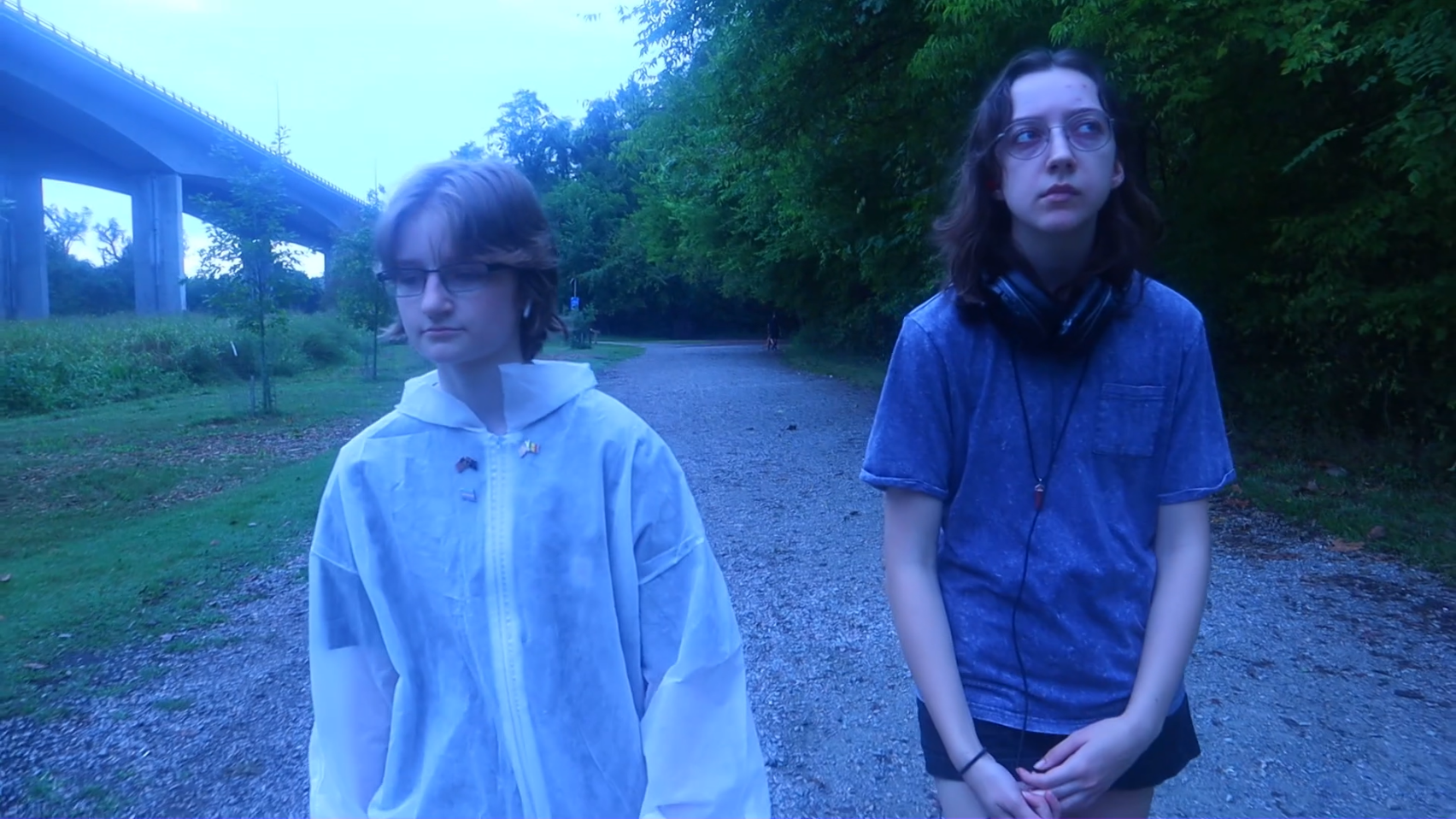 Image ID: Two people are walking forward through a blue-tinged forest path. The photograph is of their fronts.